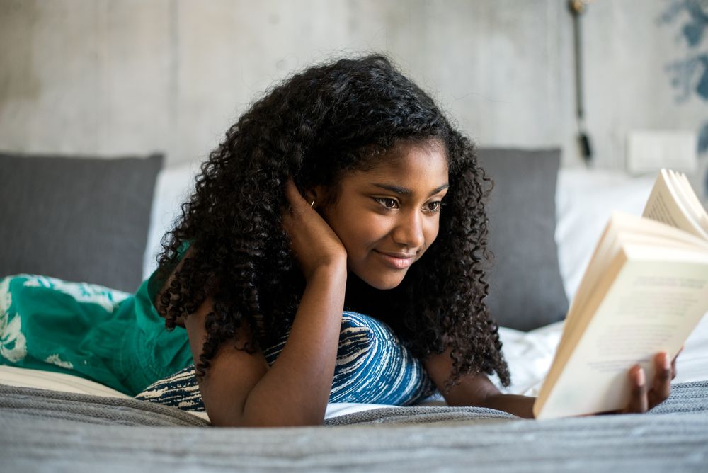 Black teenage reading a book on bed