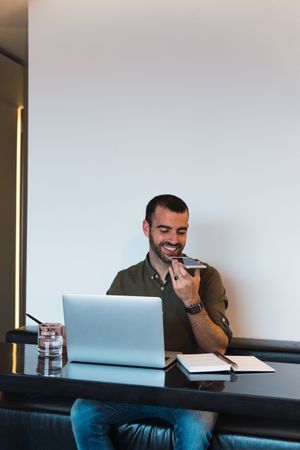 Positive man recording audio message near laptop