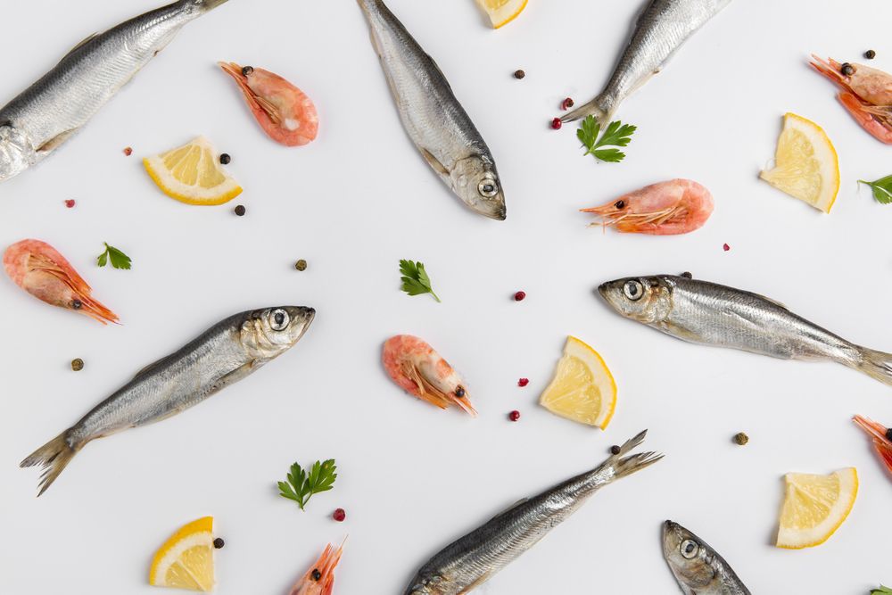 Arrangement of fish and shrimp with lemon on light background
