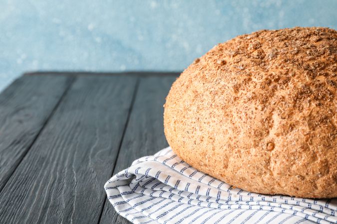 Bread on kitchen towel on wooden table against light background, space for text and closeup