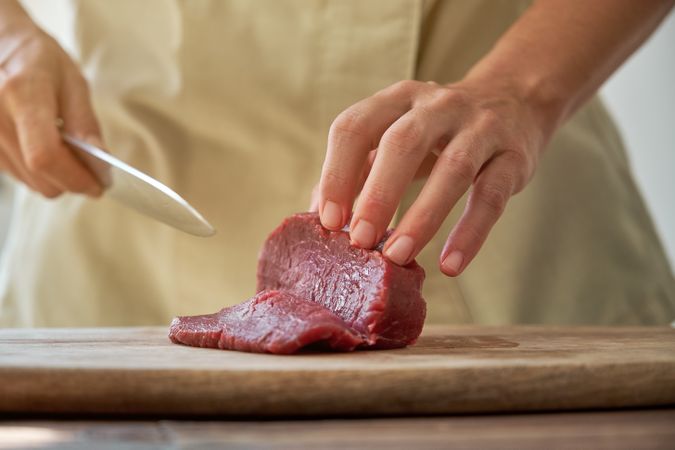 Crop woman cutting beef on board