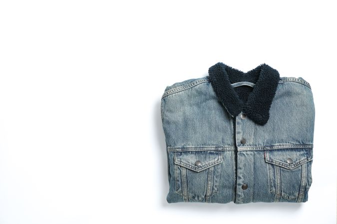 Folded denim jacket on light background, space for text