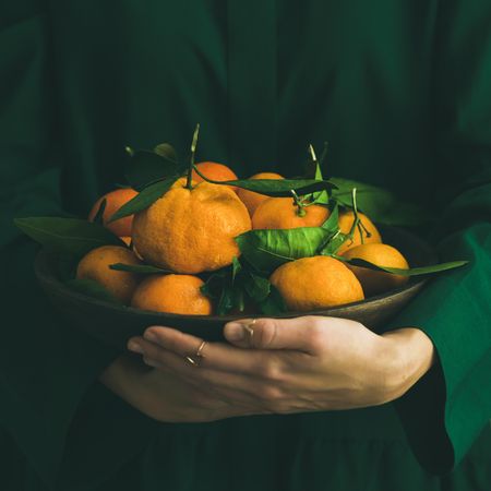 Woman in green holding bowl of tangerines, copy space, square crop