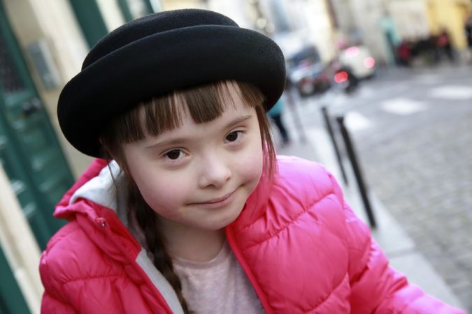 Beautiful little girl with Down syndrome wearing a pink puffer coat and hat smiling
