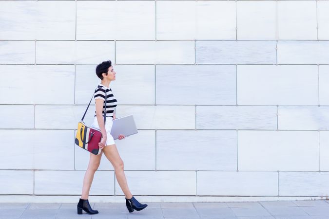 Side view of woman walking down the street with ankle boots and colorful computer bag