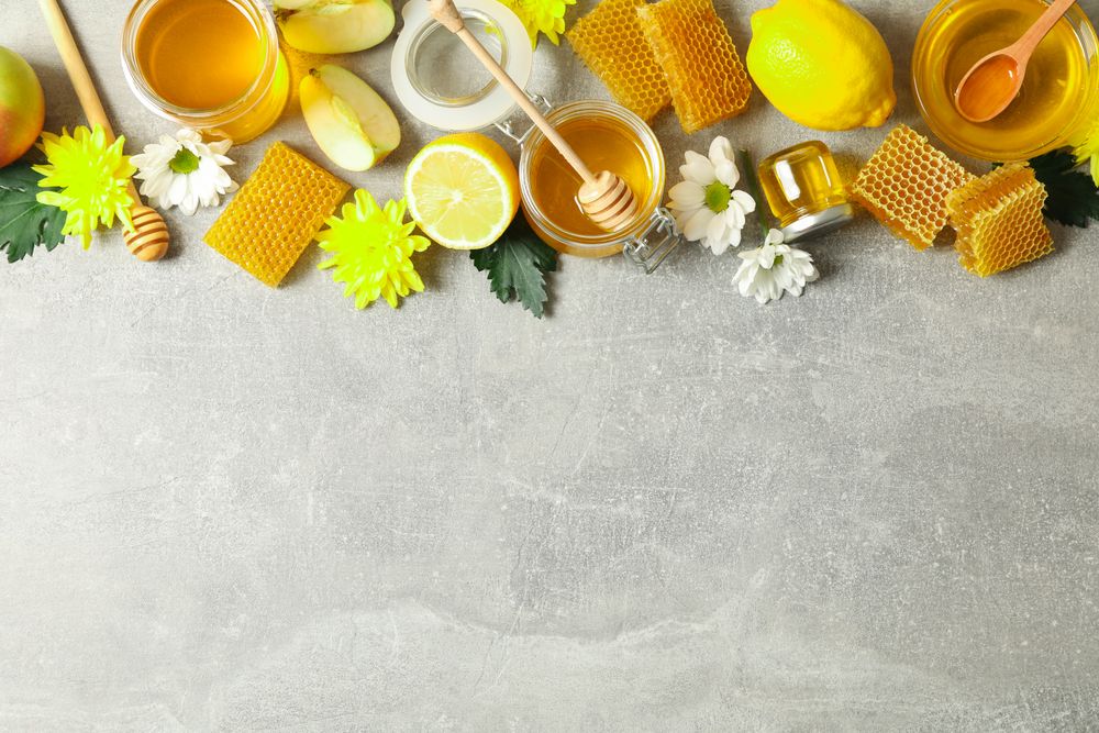 Flat lay with honey, flowers and fruits on grey background, copy space