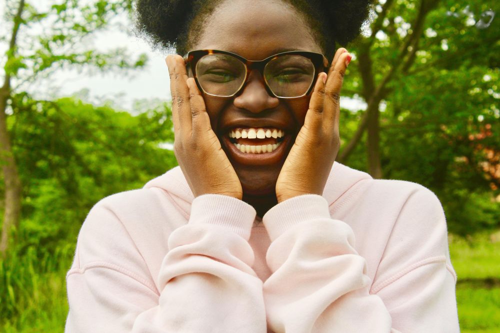 Woman with curly hair smiling and wearing eyeglasses near trees