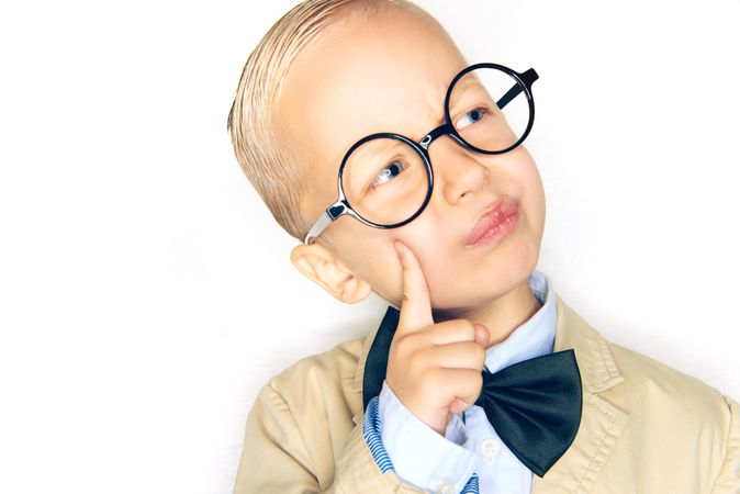 Inquisitive blond boy wearing round glasses and bow tie with finger to his cheek