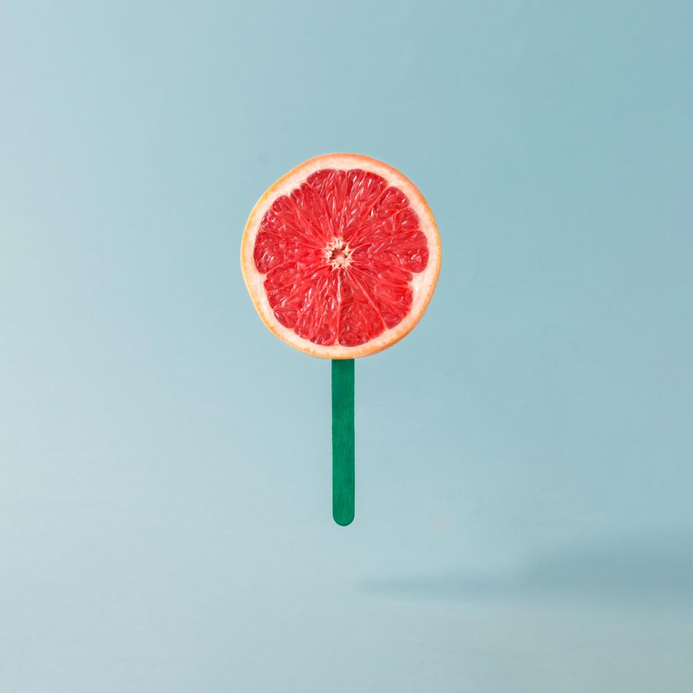 Grapefruit half with ice cream stick on pastel blue background