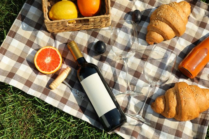 Composition with wine, croissants, fruits and towel on grass, top view