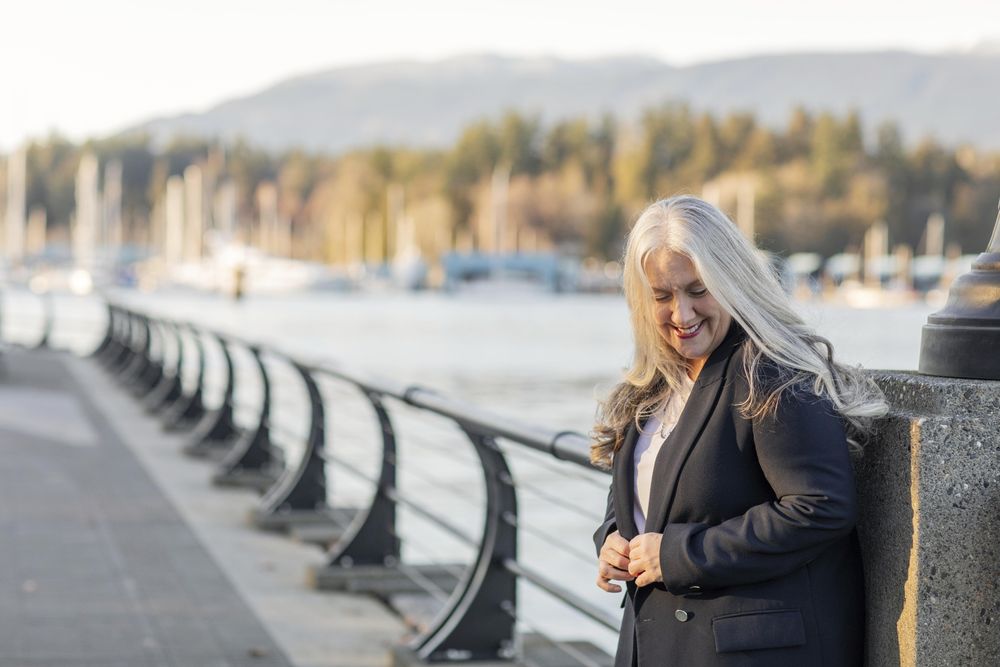 Smiling woman leaning on a lamp post buttoning blazer