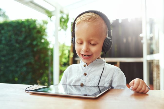 Smiling blond boy using headphones while watching show on digital tablet
