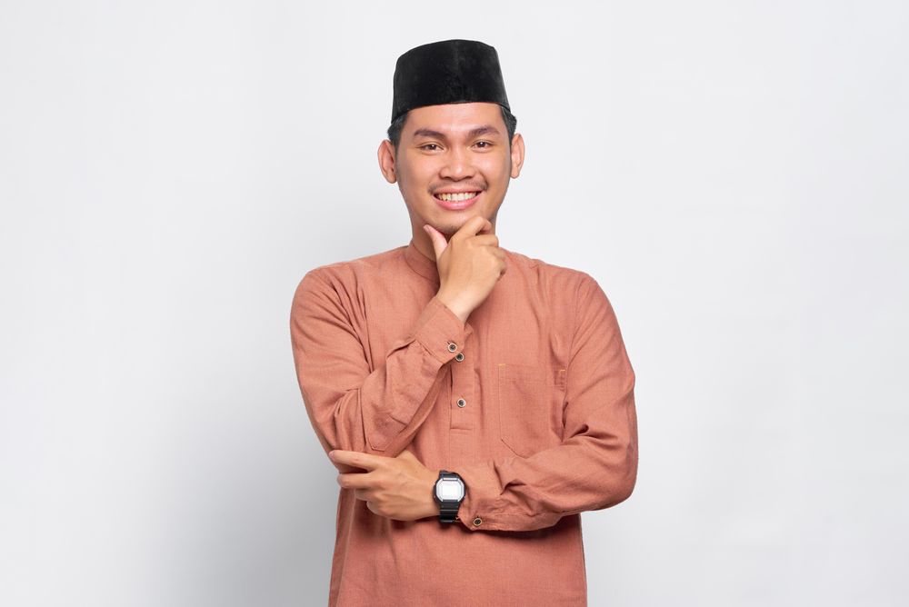 Muslim man in kufi head wear smiling with hand on chin