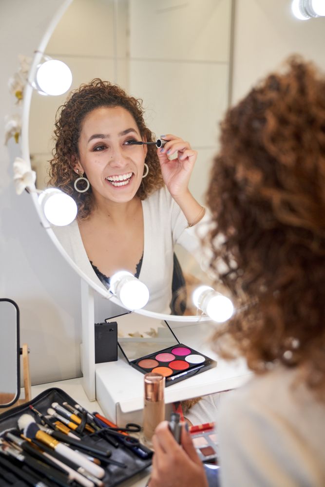 Cheerful young woman applying mascara on eyelashes while doing m