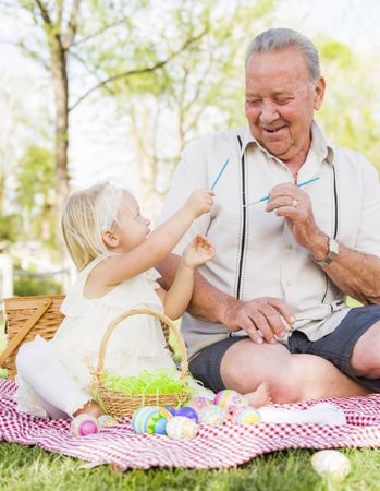 Grandfather and Granddaughter Coloring Easter Eggs on Blanket At Park
