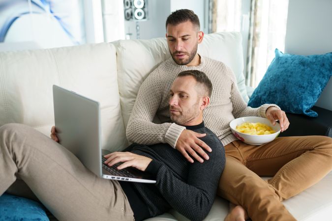Two men relaxing together reading something on laptop