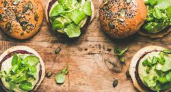 Fresh vegan burgers on seeded buns arranged on wooden board, with copy space