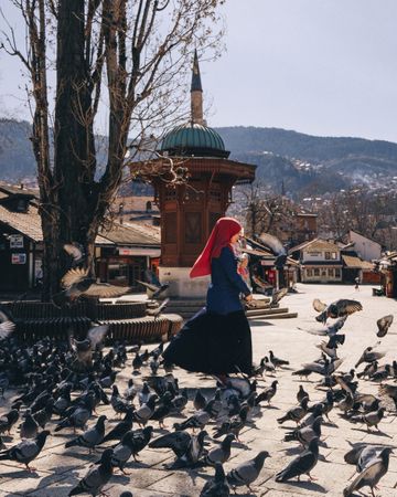 Woman wearing hijab standing among pigeons outdoor