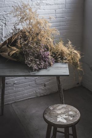 Bunch of plant in paper on table near stool in grey room