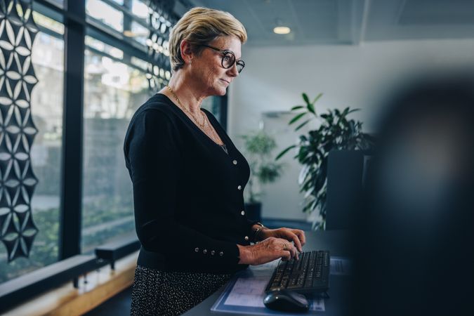Mature female professional working at standing desk in modern office