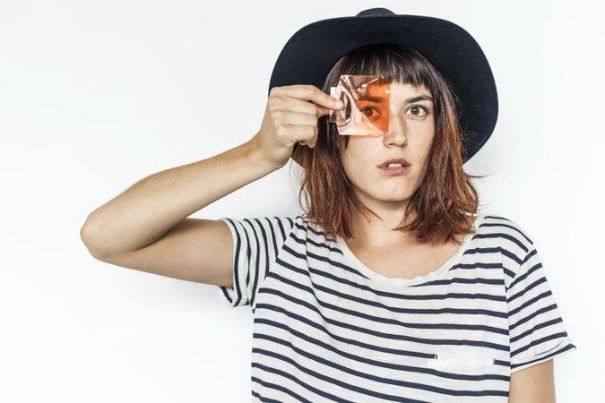 Female in striped shirt and felt hat holding transparent orange material to eye