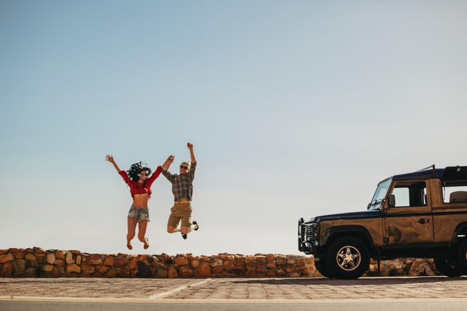 Young man and woman jumping outdoors in front of the car