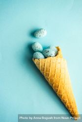 Waffle cone with blue speckled eggs on blue pastel background bYqGed