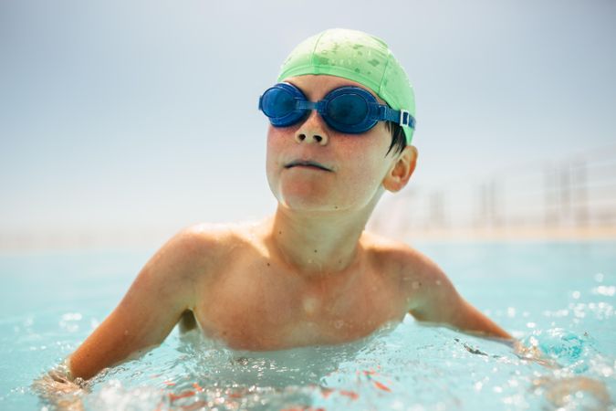Boy with swim cap and goggles swimming in pool