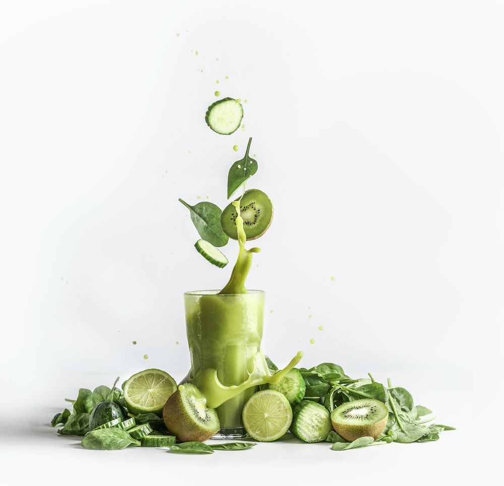 Splashing of green smoothie in glass with and flying ingredients: cucumber,kiwi and spinach leaves