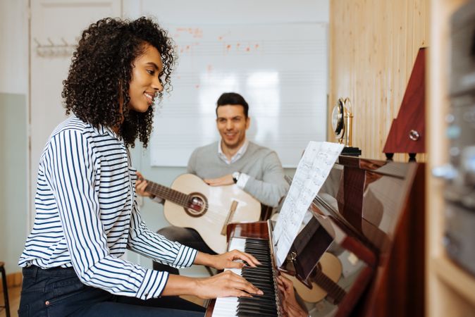 Woman playing piano near man playing guitar in studio