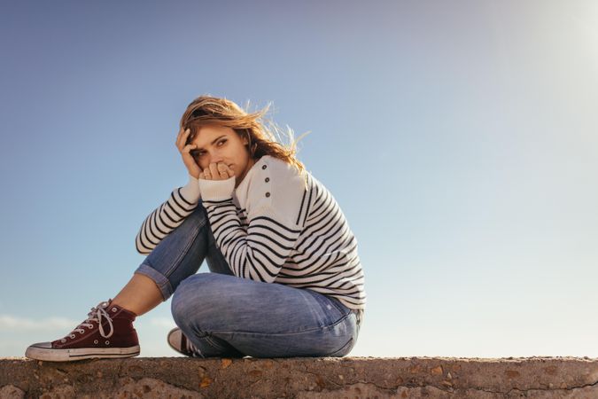 Young woman sitting on concrete wall and looking away