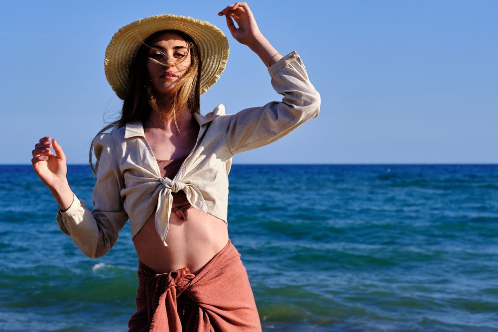 A fashion model with a hat at the beach before sunset