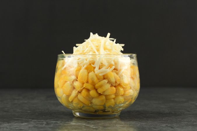 Side view of glass cup of Indonesian sweet corn snack grated cheese