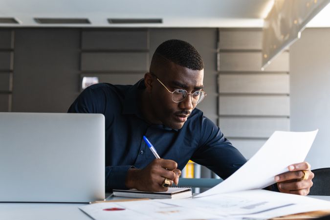 Black male writing in notepad near laptop in office