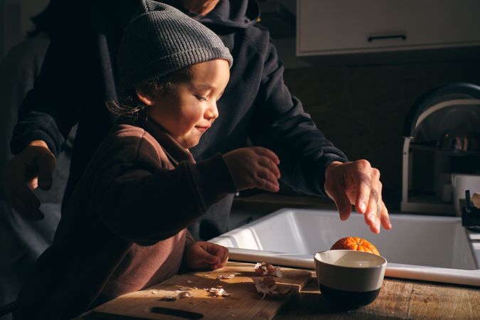 Cute little boy peeling citruses with help of unrecognizable fat