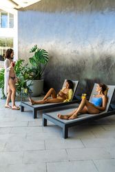 Two women friends chat while resting on a lounge seat when they unexpectedly run into an acquaintance. Vertical shot