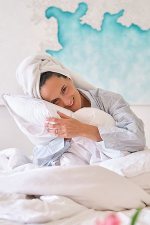 Dreamy female hugging pillows on bed at home