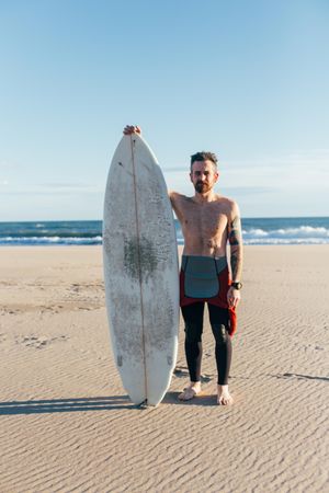 Portrait of surfer in wetsuit with surfboard, vertical