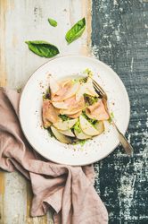 Top view of ham and pear in bowl, on blue painted wooden background with linen napkin