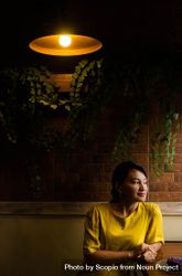 Woman in yellow dress sitting under lamp in front of brick wall 4NxB80