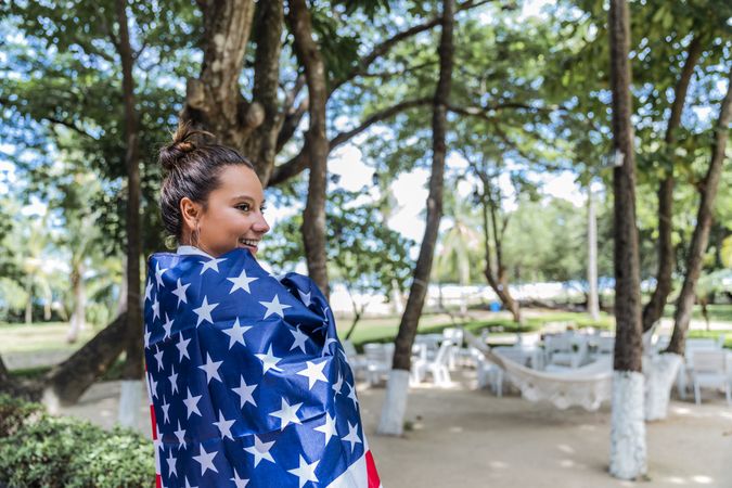 Content woman smiling wrapped in American flag walking along park