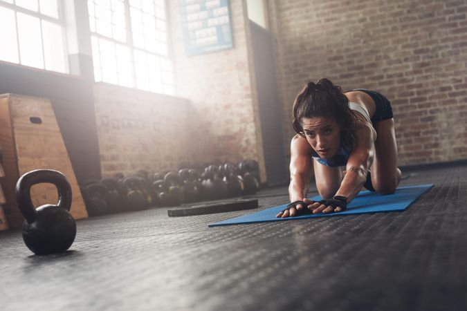 Portrait of determined young female athlete working out on exercise mat at gym