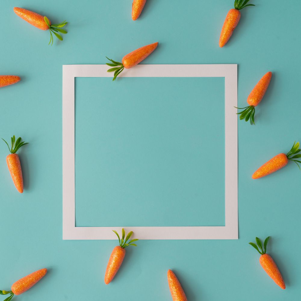Easter pattern made with carrots on bright blue background with paper square outline