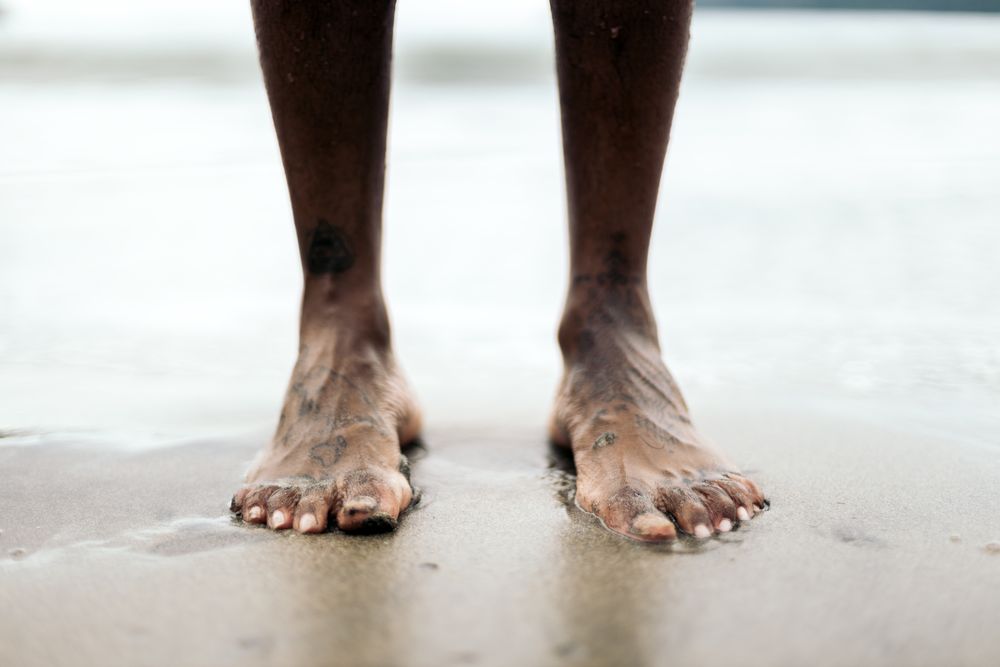 Tattooed feet on the sand on the beach.