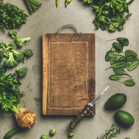 Arrangement of fresh green garden vegetables on concrete surface, with wooden board, square crop