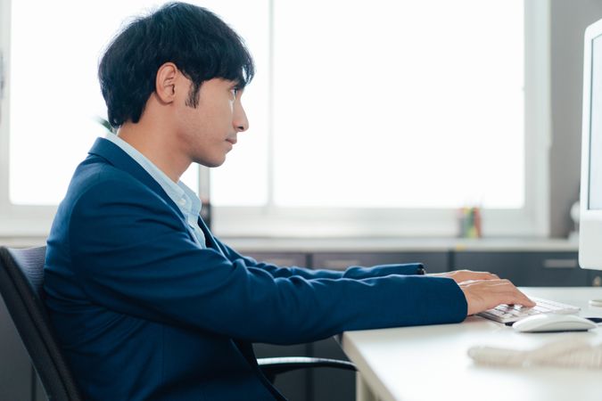 Side view of Asian male in suit at work computer