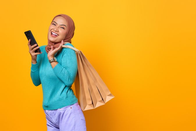 Happy Muslim woman with shopping bags on her back and phone in her hand