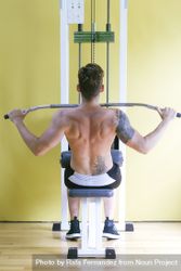 Back of tattooed male pulling down bar to his chest on weight machine 0glnX5