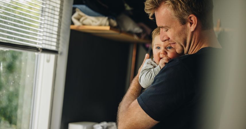 Loving father holding adorable baby in nursery room