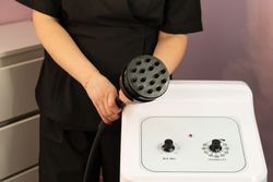 Therapist presenting cavitation handpiece above aesthetic control panel
